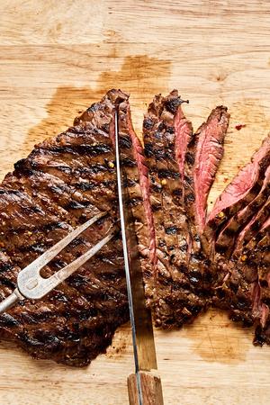 grilled skirt steak being sliced thinly on a cutting board