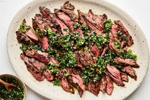 sliced grilled skirt steak on a platter topped with Chimichurri sauce