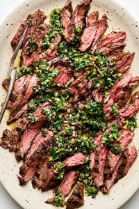 sliced grilled skirt steak on a platter topped with Chimichurri sauce