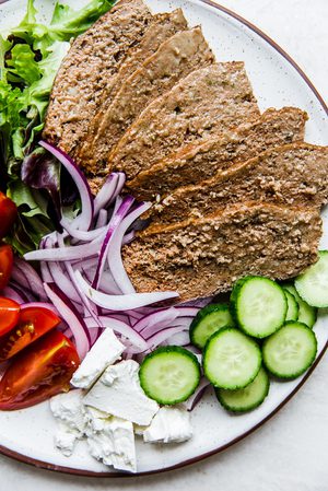 Homemade gyro meat sliced on a platter with cucumbers, feta, tomatoes, onions