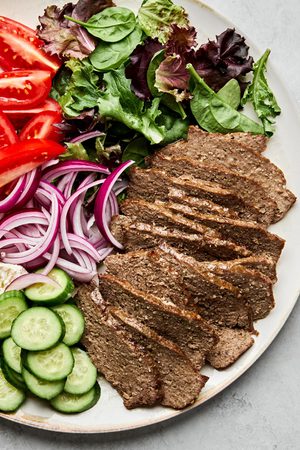 Platter of homemade gyro meat served with fresh lettuce, tomato, red onion, cucumber, and feta cheese