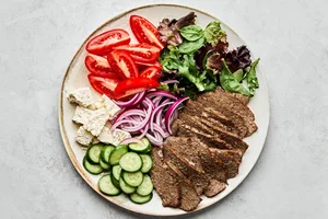 Platter of homemade gyro meat served with fresh lettuce, tomato, red onion, cucumber, and feta cheese