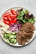 Platter of homemade gyro meat served with fresh lettuce, tomato, red onion, cucumber, and feta cheese