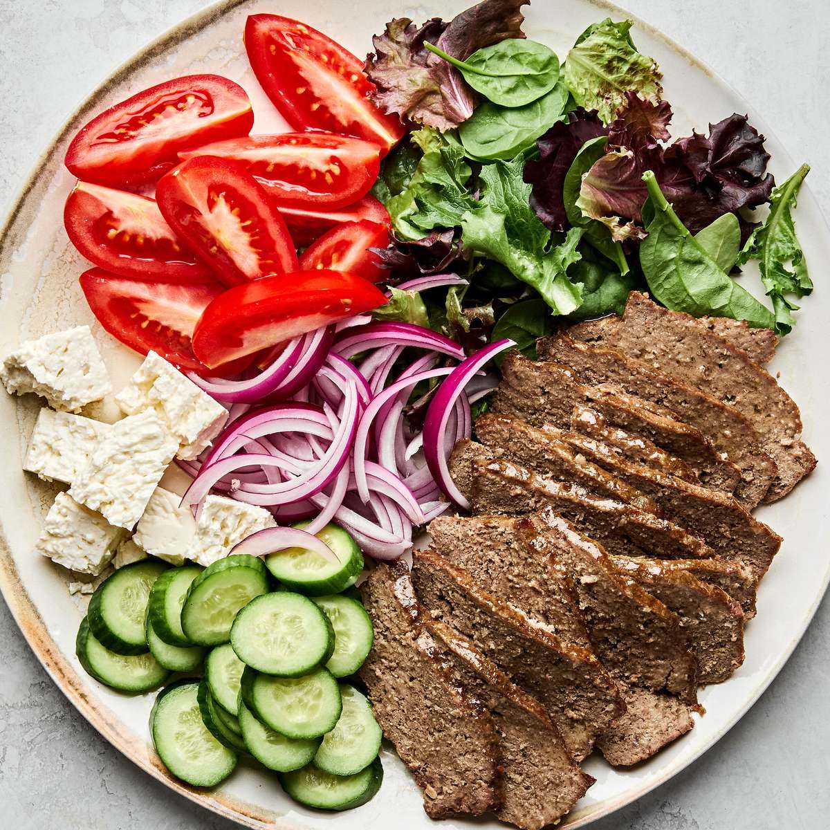 Platter of homemade gyro meat served with fresh lettuce, tomato, red onion, cucumber, and feta cheese