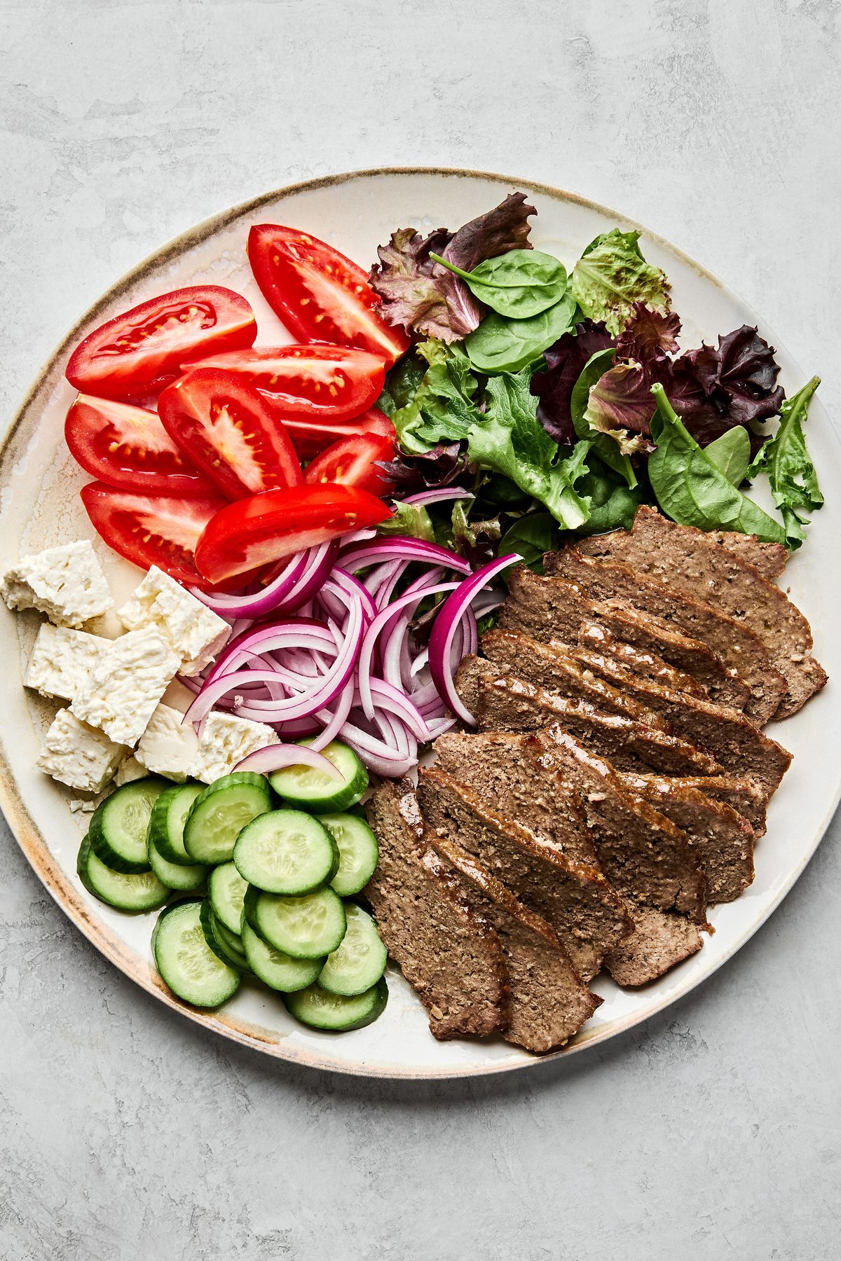 Platter of homemade gyro meat served with fresh lettuce, tomato, red onion, cucumber, and feta cheese