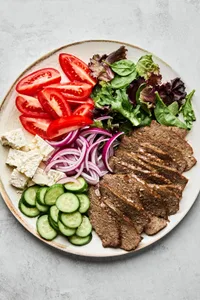 Platter of homemade gyro meat served with fresh lettuce, tomato, red onion, cucumber, and feta cheese