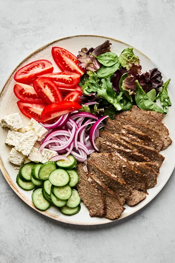 Platter of homemade gyro meat served with fresh lettuce, tomato, red onion, cucumber, and feta cheese