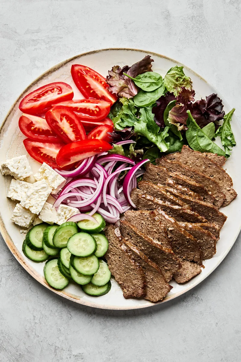 Platter of homemade gyro meat served with fresh lettuce, tomato, red onion, cucumber, and feta cheese