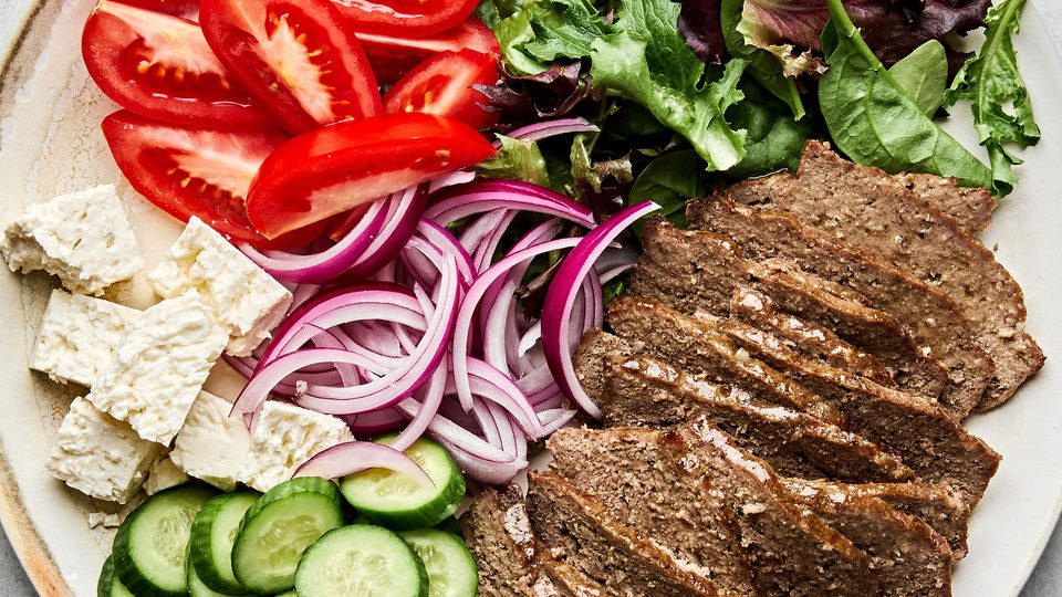 Platter of homemade gyro meat served with fresh lettuce, tomato, red onion, cucumber, and feta cheese