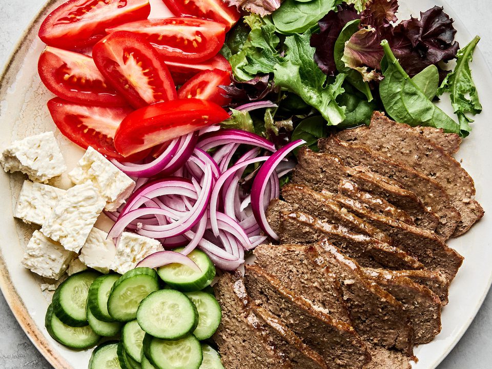 Platter of homemade gyro meat served with fresh lettuce, tomato, red onion, cucumber, and feta cheese