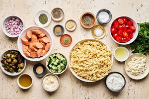 pasta, Italian sausage, greek olives, tomatoes, cucumbers, red onion, parsley, feta, olive oil, salt & pepper in prep bowls