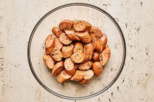 sliced Italian sausage being tossed with  thyme, granulated garlic, cumin, oregano, pepper, salt, and olive oil