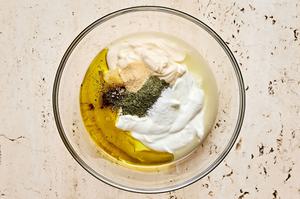 Greek yogurt, mayonnaise, olive oil, garlic, lemon juice, dill, granulated garlic, salt, and pepper being combined in a bowl