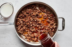 stock and milk being added to a skillet with ground beef, butter, tomato paste and spices