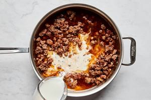 milk being poured into a skillet with ground beef, spices, and stock