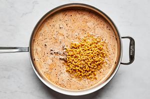 cooked macaroni noodles being stirred into a skill with cooked ground beef and creamy sauce