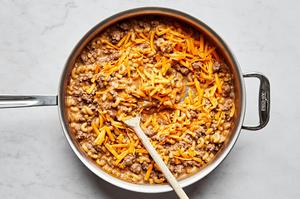 shredded cheddar cheese being stirred into a pan of homemade hamburger helper