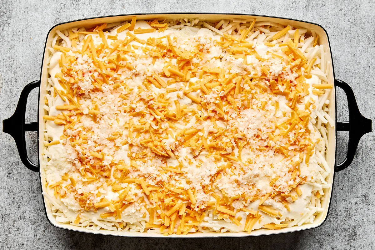 hashbrown casserole with a cream potato mixture topped with shredded cheese ready for the oven