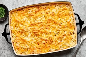 A golden-brown hashbrown casserole in a baking dish, with a creamy potato filling topped with melted cheese and chives