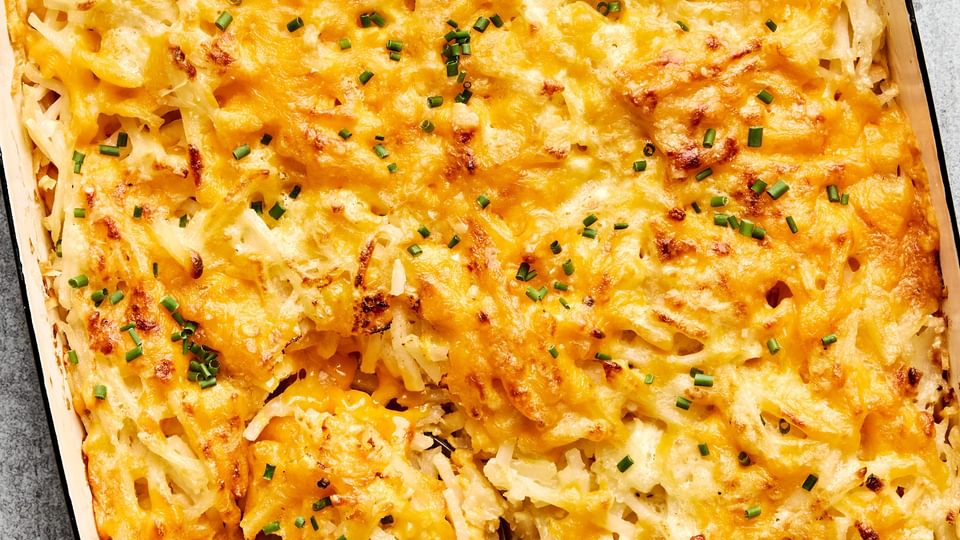 A golden-brown hashbrown casserole in a baking dish, with a creamy potato filling topped with melted cheese and chives