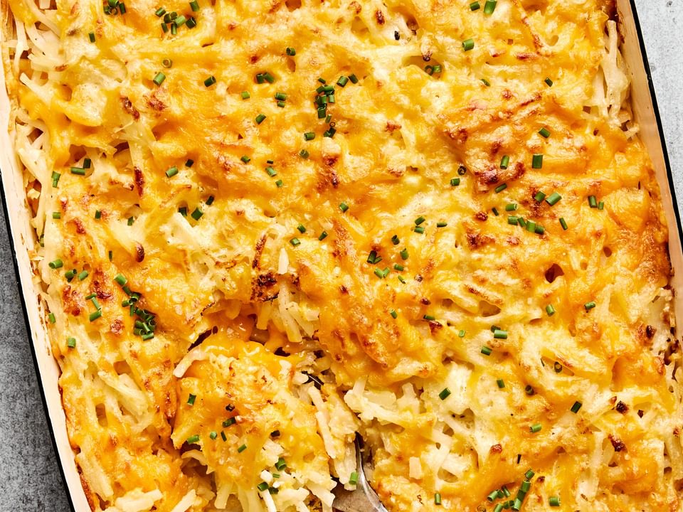 A golden-brown hashbrown casserole in a baking dish, with a creamy potato filling topped with melted cheese and chives