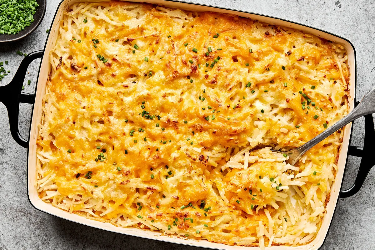 A golden-brown hashbrown casserole in a baking dish, with a creamy potato filling topped with melted cheese and chives