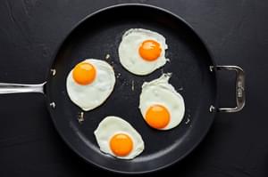 4 eggs being fried in a skillet
