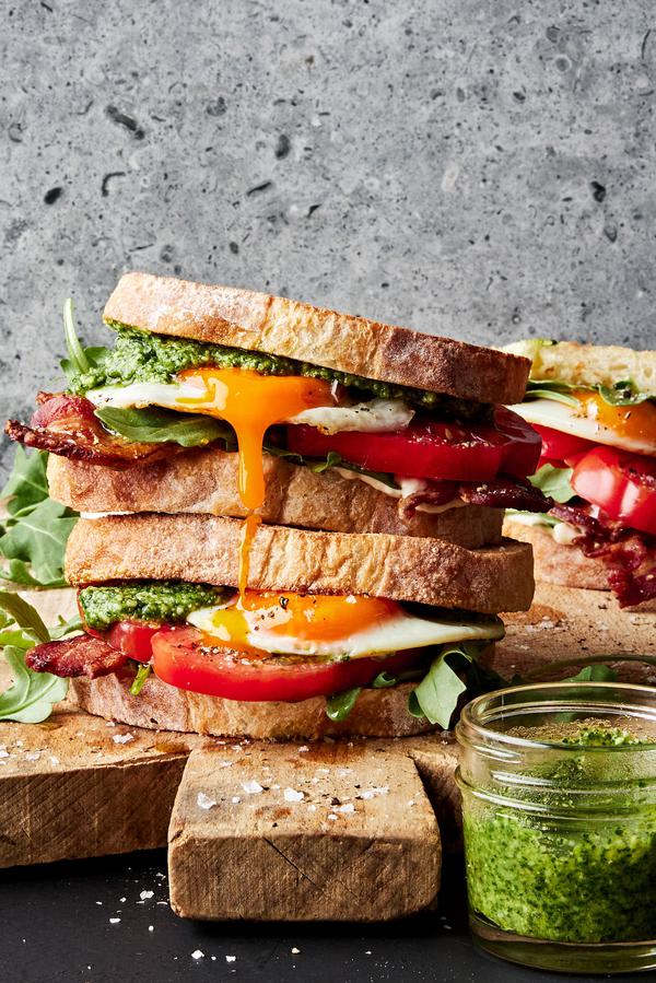 a homemade heirloom BLT with pesto and a fried egg stacked on a cutting board