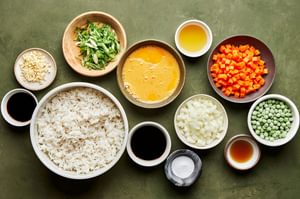 ingredients for fried rice laid out in bowls: rice, eggs, veggies, sesame oil, coconut aminos and soy sauce