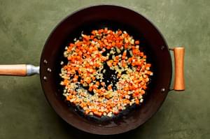 onion and carrot being cooked in vegetable oil in a wok