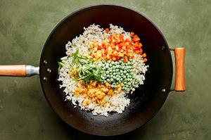 rice, onion, eggs, carrots, garlic, peas, being fried in a wok