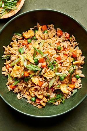 a bowl of homemade fried rice made with onion, eggs, carrots, garlic, peas, sesame oil and soy sauce topped with green onion