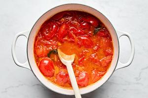 tomatoes, olive oil, salt, garlic and fresh basil being stirred in a pot to make homemade tomato sauce