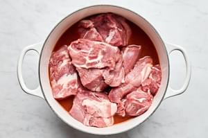pork shoulder chunks being added to a dutch oven with homemade honey chipotle sauce