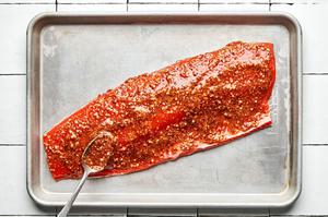 raw salmon fillet on a baking sheet covered with marinade made of mustard, honey, garlic, salt, paprika and pepper.
