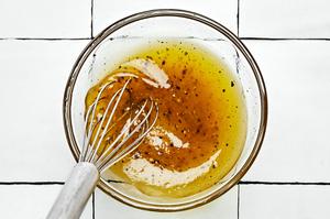 olive oil, lemon zest, lemon juice, honey, salt, and pepper being whisked in a bowl