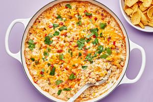 hot corn dip in a skillet made with cream cheese, sour cream, mayo, cheese & spices topped with cilantro served with fritos