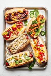 a platter of hot dogs with multiple toppings like hawaiian, italian-american , mexican, banh mi, chicago and the deli dog
