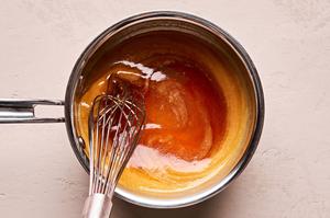 honey and apple cider vinegar being whisked into melted butter and sriracha in a small pot
