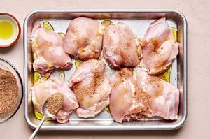 raw chicken thighs, patted dry, drizzled with olive oil and being sprinkled with spices