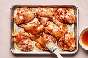 raw chicken thighs seasoned being brushed with hot honey sauce