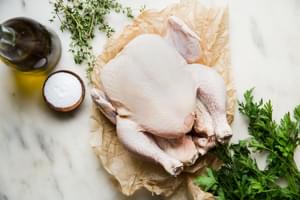 a whole chicken on parchment paper with parsley, thyme, salt and olive oil