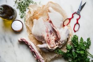 the back bone cut out of a whole chicken on parchment paper with salt, olive oil, thyme and parsley