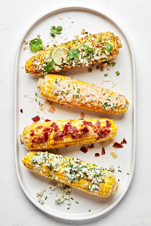 4 grilled corn on the cob with different toppings: maple bourbon butter, chipotle mayo, spicy cotija cheese, & blue cheese