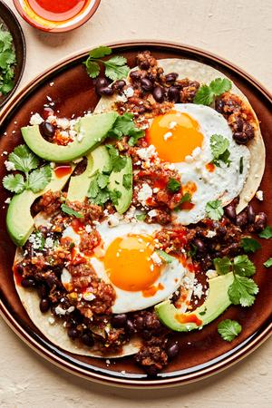 homemade huevos rancheros. fried eggs over seasoned beans and corn tortillas topped with cilantro, avocado and cotija
