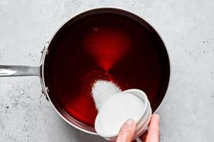 sugar being poured into a pot of black tea concentrate