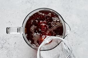 cold water being poured into a pitcher of sweetened black tea concentrate