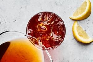 homemade iced tea being poured into a glass with ice with lemon wedges beside for garnish