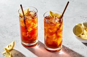 2 glasses of homemade iced tea with a metal straws sweetened with simple syrup and garnished with a lemon wedge