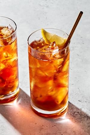 2 glasses of homemade iced tea with a metal straws sweetened with simple syrup and garnished with a lemon wedge